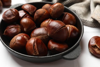 Fresh edible sweet chestnuts in frying pan on white tiled table, closeup