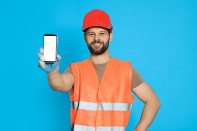 Man in reflective uniform showing smartphone on light blue background