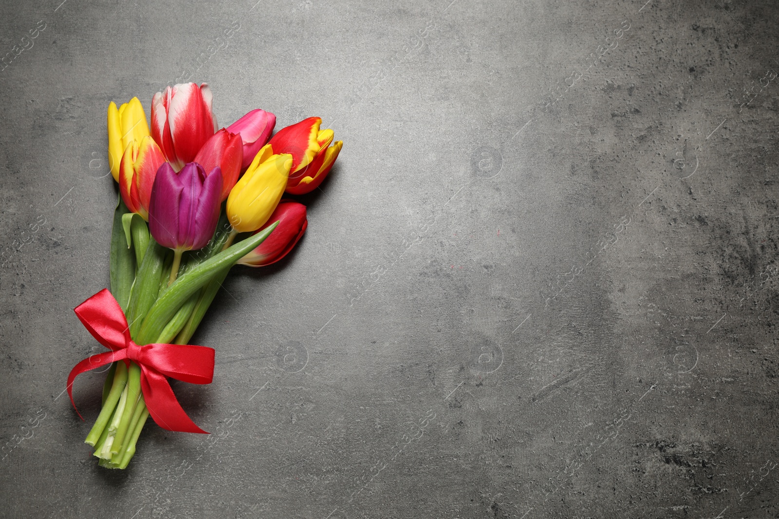 Photo of Beautiful spring tulips on grey stone table, top view. Space for text
