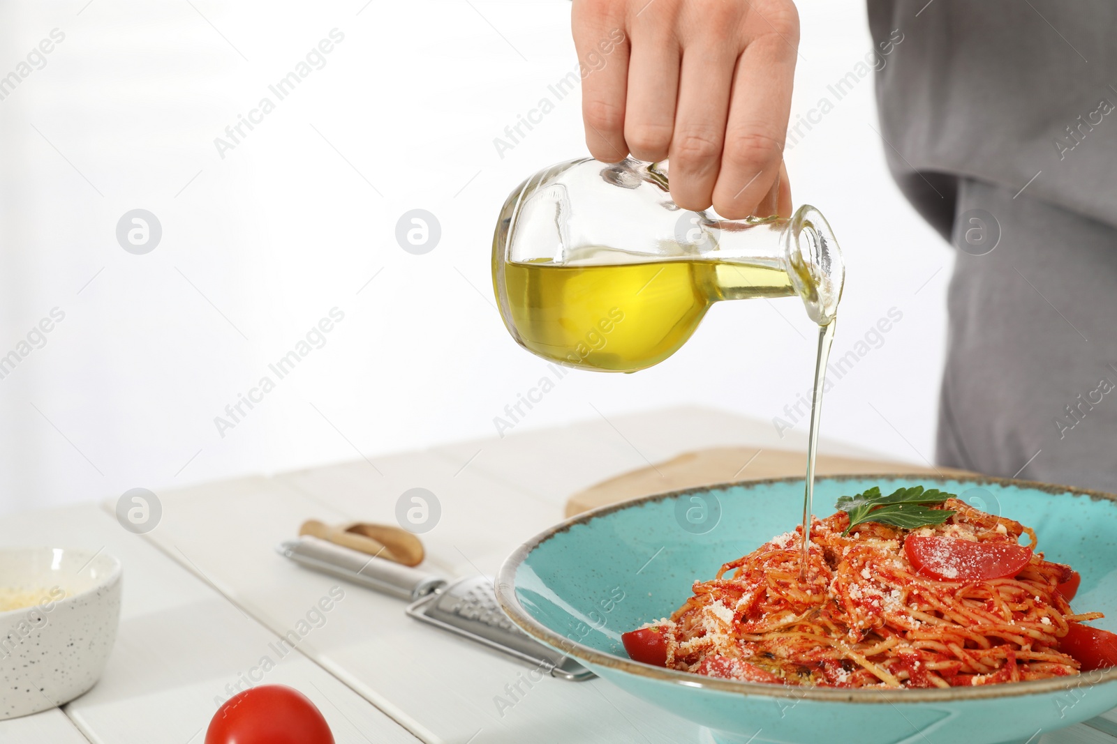 Photo of Food stylist pouring oil into spaghetti at white wooden table in photo studio, closeup