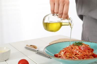 Photo of Food stylist pouring oil into spaghetti at white wooden table in photo studio, closeup