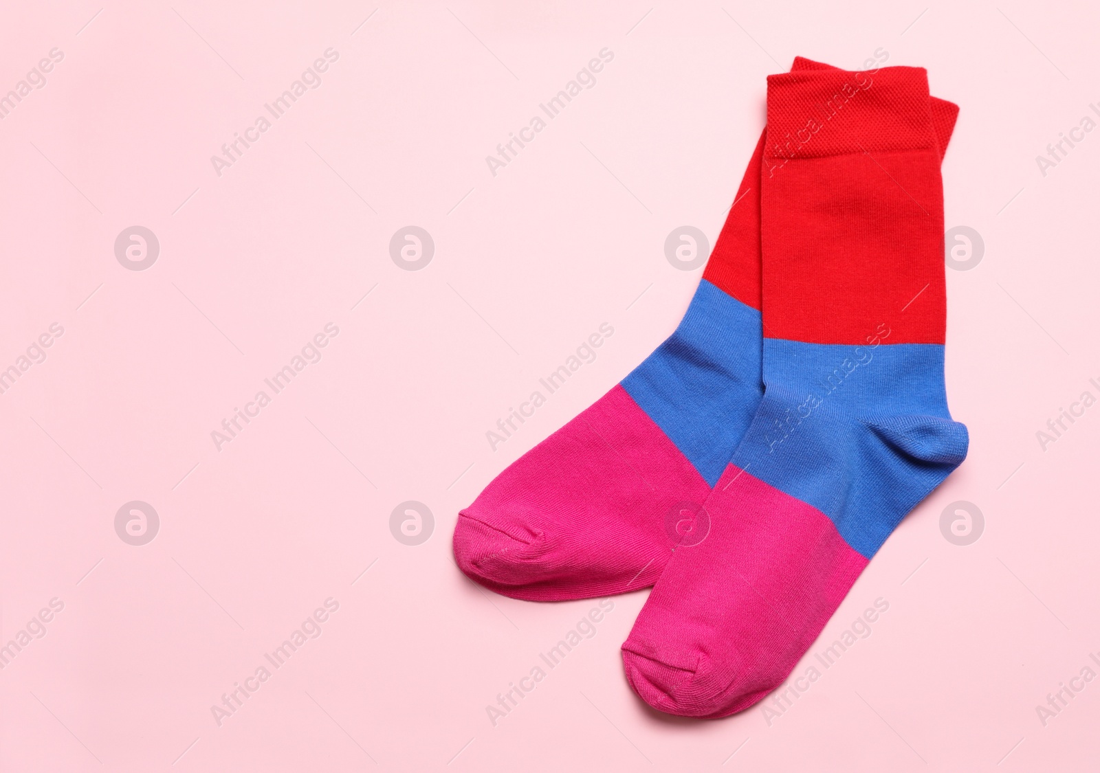 Photo of Colorful striped socks on light pink background, flat lay. Space for text