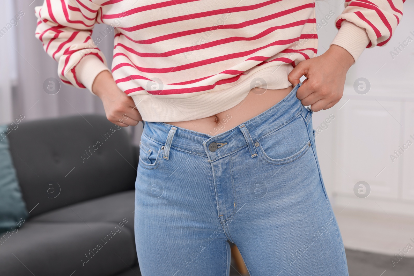 Photo of Woman trying to fit into her jeans at home, closeup