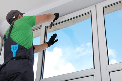 Photo of Worker installing double glazing window indoors, low angle view