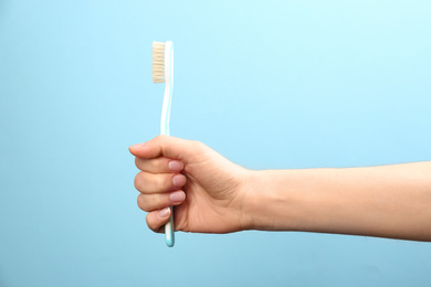 Photo of Woman holding toothbrush with natural bristles on light blue background, closeup