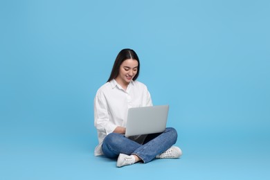 Photo of Smiling young woman working with laptop on light blue background. Space for text