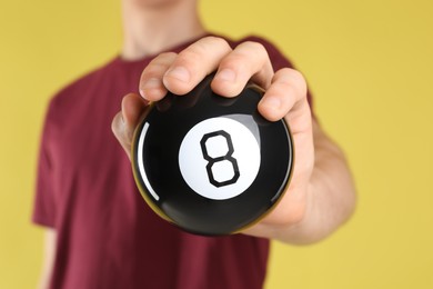 Photo of Man holding magic eight ball on yellow background, closeup