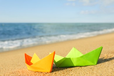 Bright color paper boats on sandy beach near sea