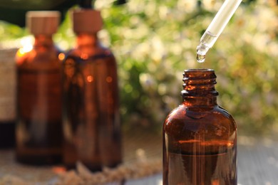 Photo of Dripping chamomile essential oil from pipette into bottle on blurred background, closeup. Space for text