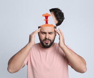 Young man having headache on light background. Illustration of atomic explosion representing severe pain