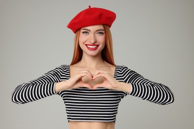 Young woman making heart with hands on light grey background