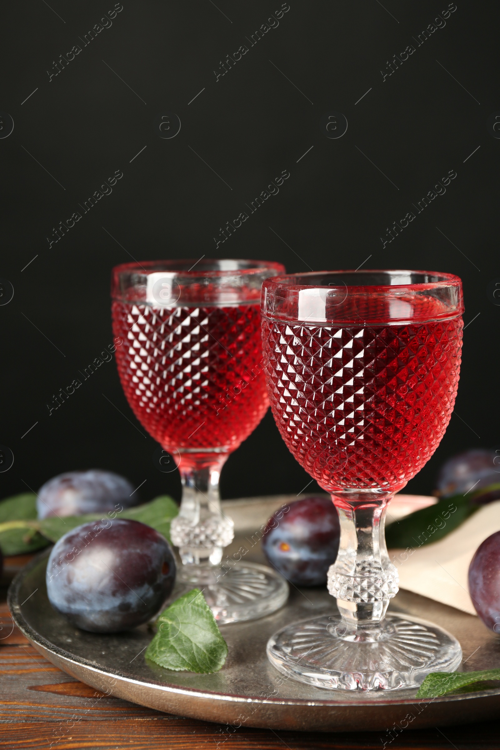 Photo of Delicious plum liquor and ripe fruits on wooden table against black background. Homemade strong alcoholic beverage