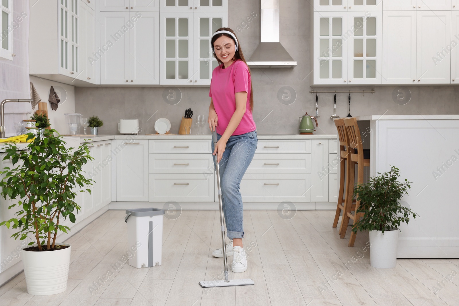 Photo of Enjoying cleaning. Happy woman in headphones listening music and mopping floor in kitchen