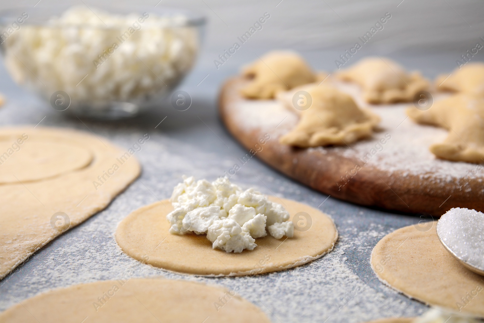 Photo of Process of making dumplings (varenyky) with cottage cheese. Raw dough and ingredients on grey table, closeup