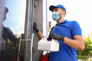 Photo of Courier in protective mask and gloves with order near front door. Restaurant delivery service during coronavirus quarantine