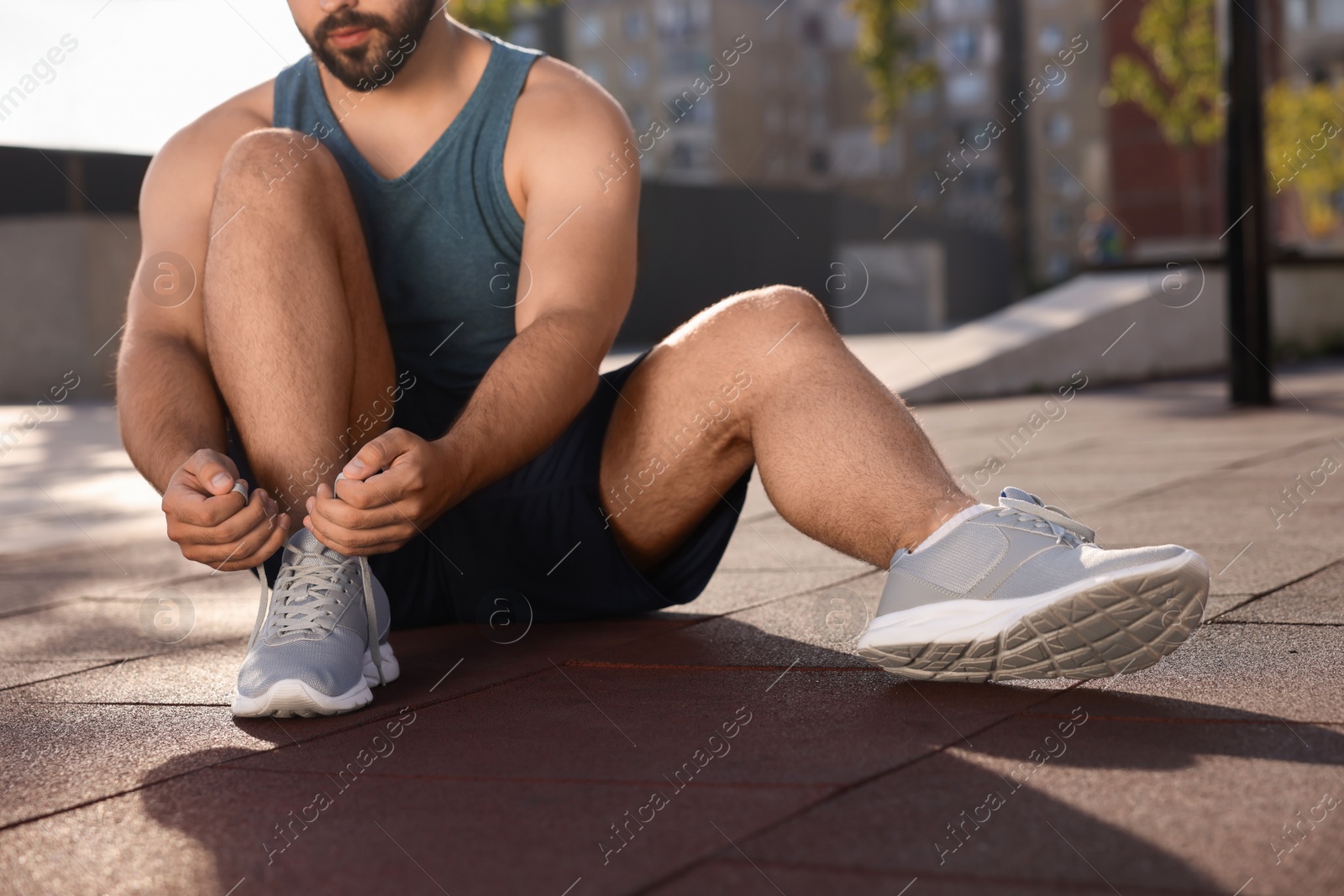 Photo of Man tying shoelaces before running outdoors on sunny day, closeup