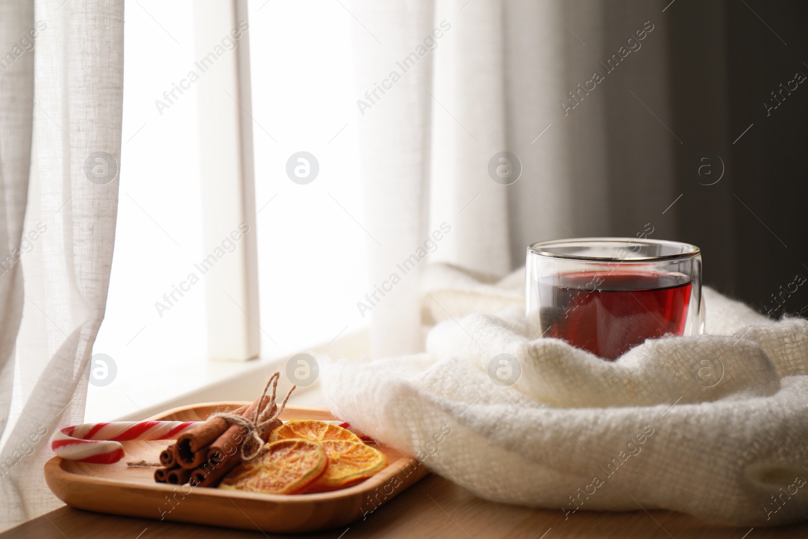 Photo of Cup of hot winter drink and scarf on wooden sill near window. Space for text