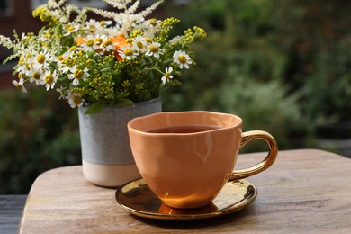 Cup of delicious chamomile tea and fresh flowers outdoors on sunny day
