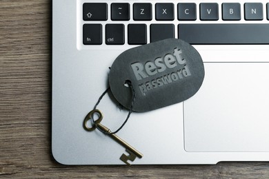 Image of Key with tag RESET PASSWORD and laptop on wooden table, top view