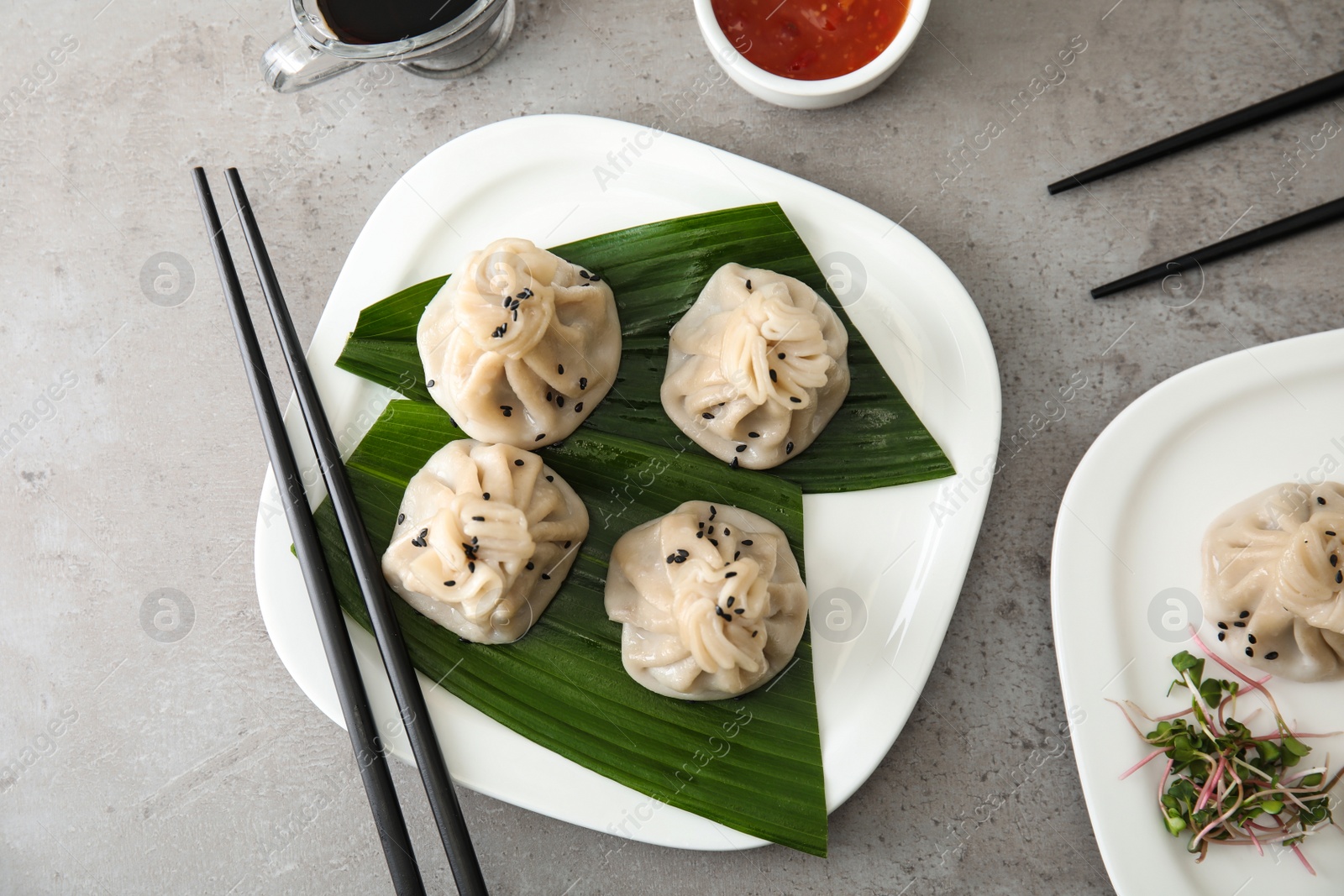 Photo of Plate with tasty baozi dumplings and chopsticks on grey table, top view