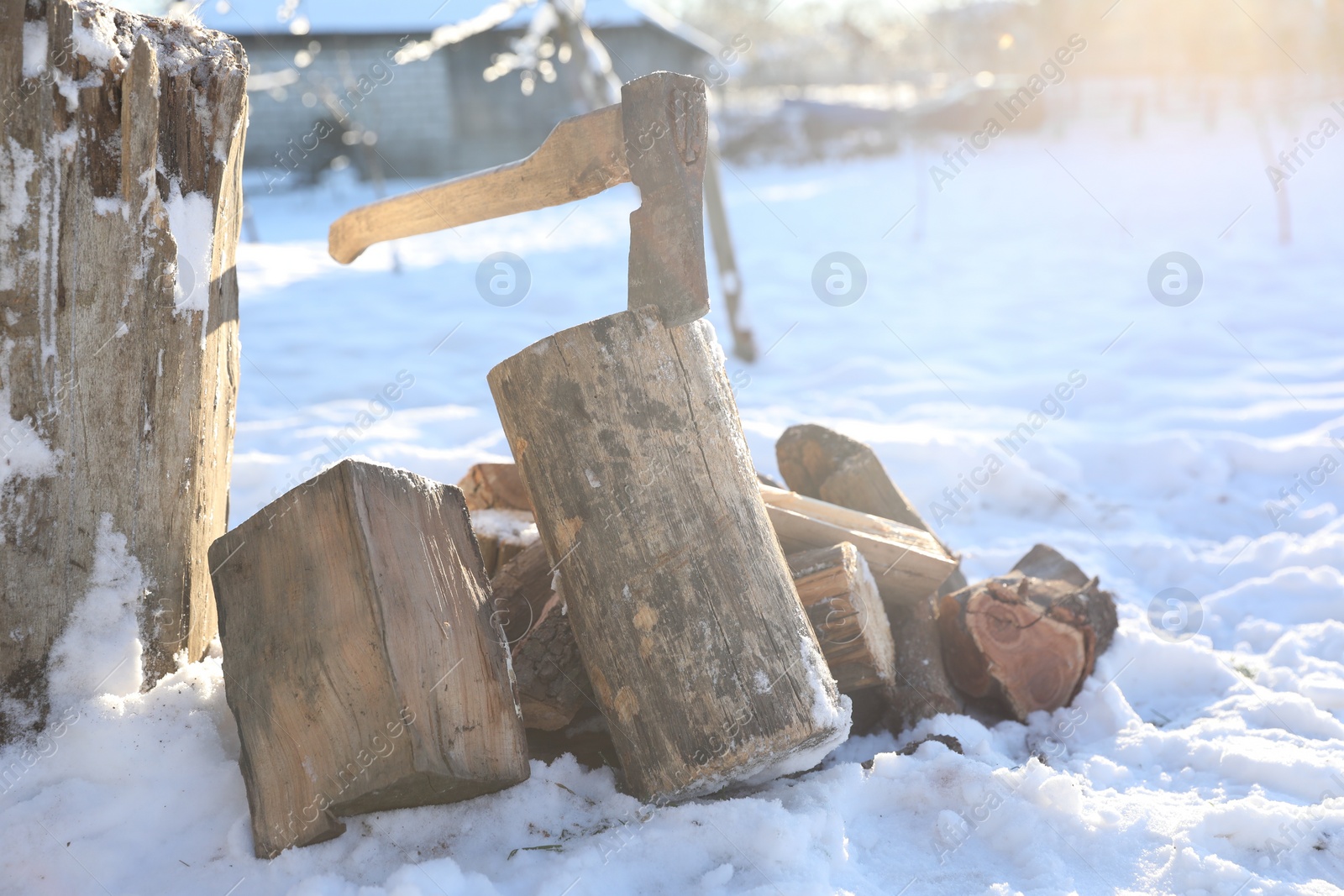 Photo of Metal axe in wooden log and pile of wood outdoors on sunny winter day