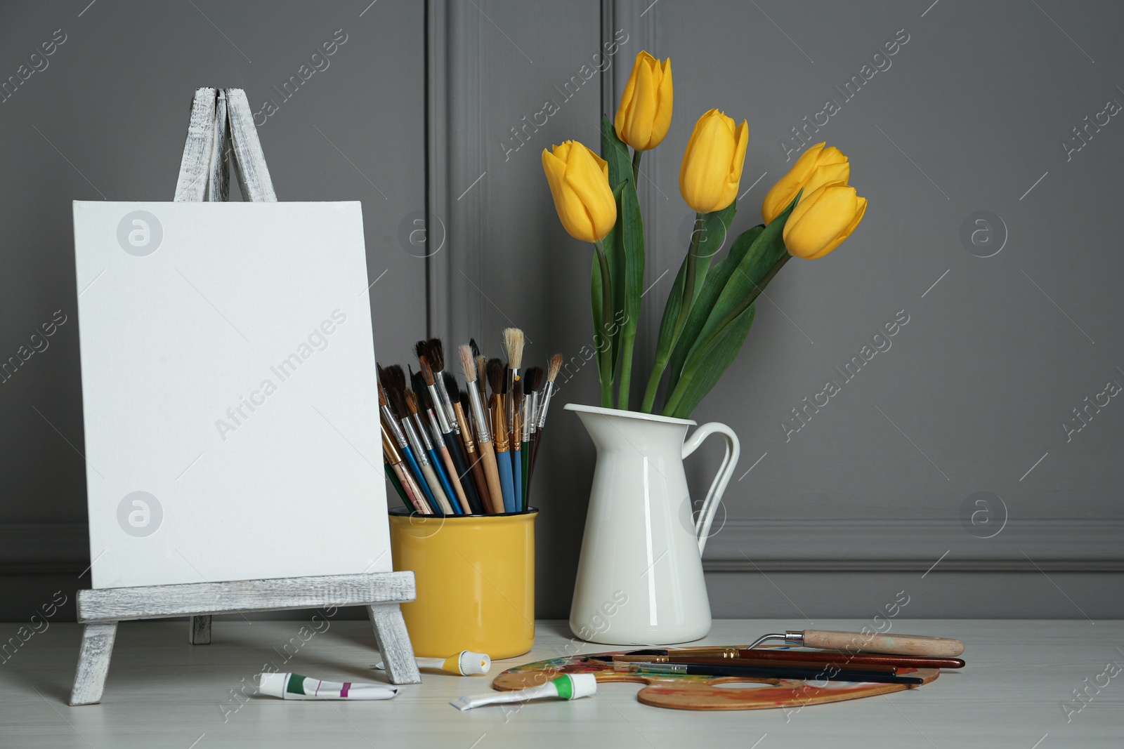 Photo of Easel with blank canvas, brushes, paints and palette in studio