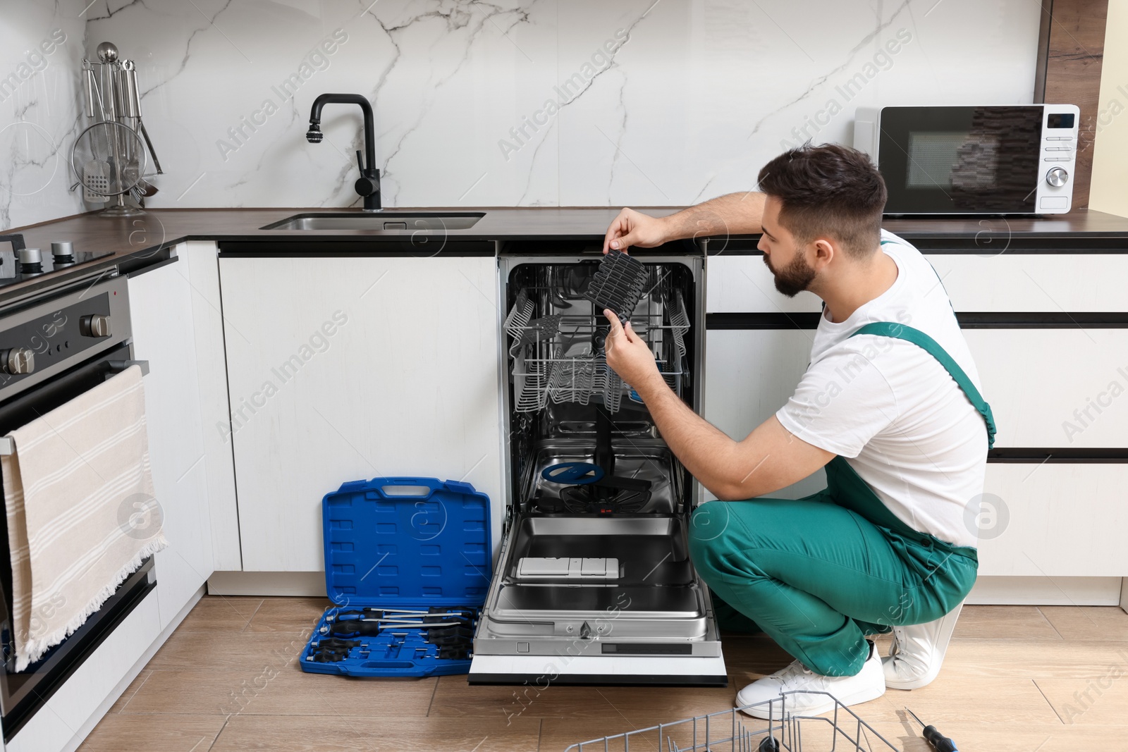 Photo of Serviceman examining dishwasher cutlery rack in kitchen