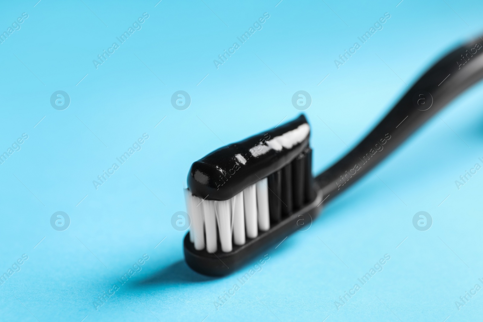 Photo of Brush with charcoal toothpaste on light blue background, closeup