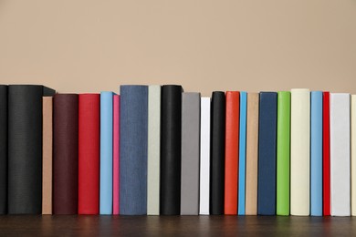 Photo of Many hardcover books on wooden table near beige wall