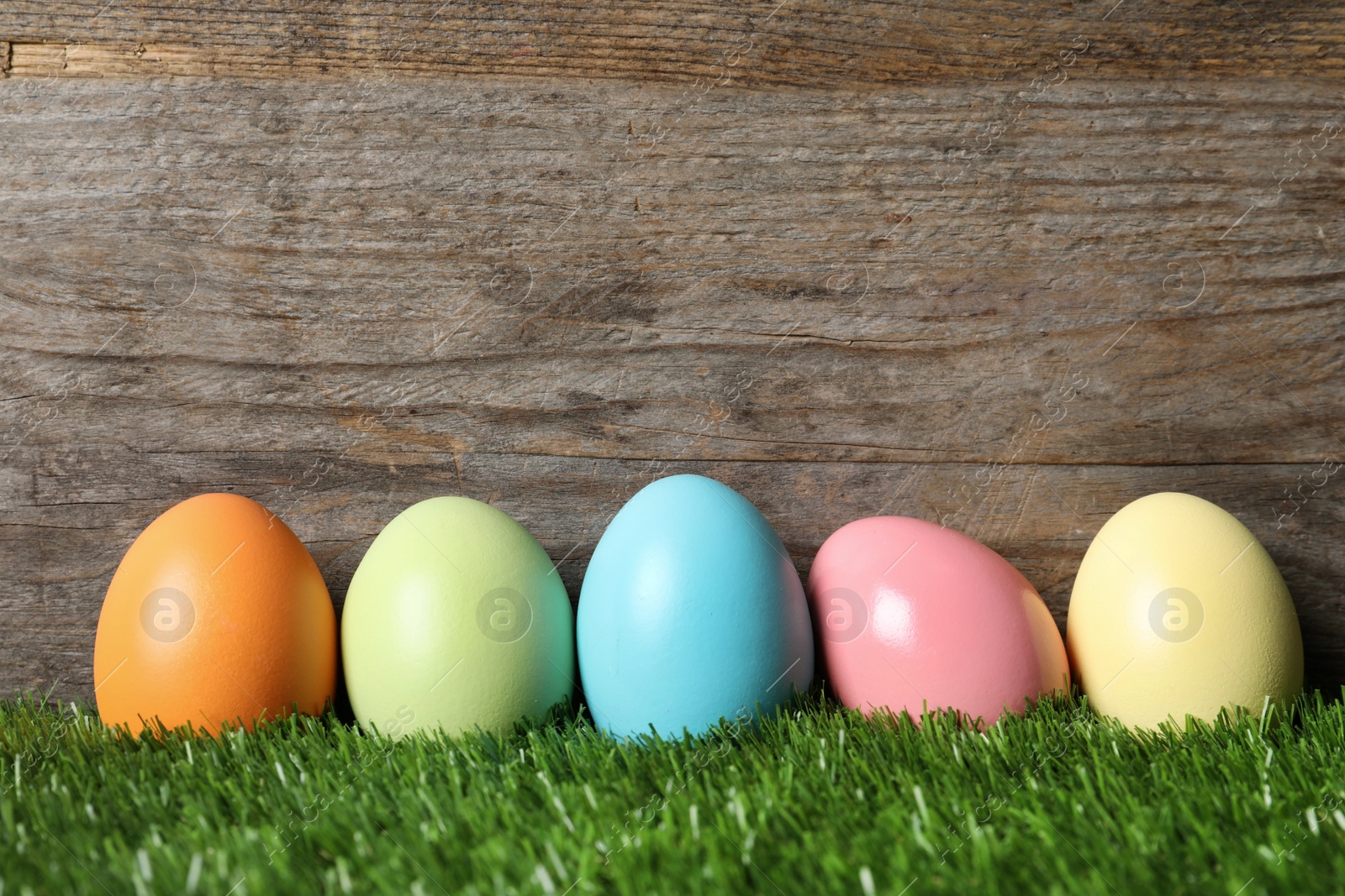 Photo of Colorful dyed Easter eggs on green grass against wooden background, space for text