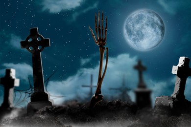 Image of Scary skeleton rising out of grave at misty cemetery