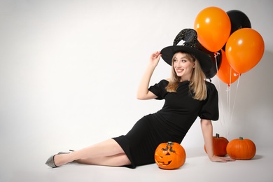 Photo of Beautiful woman in witch costume with balloons and pumpkins on white background, space for text. Halloween party