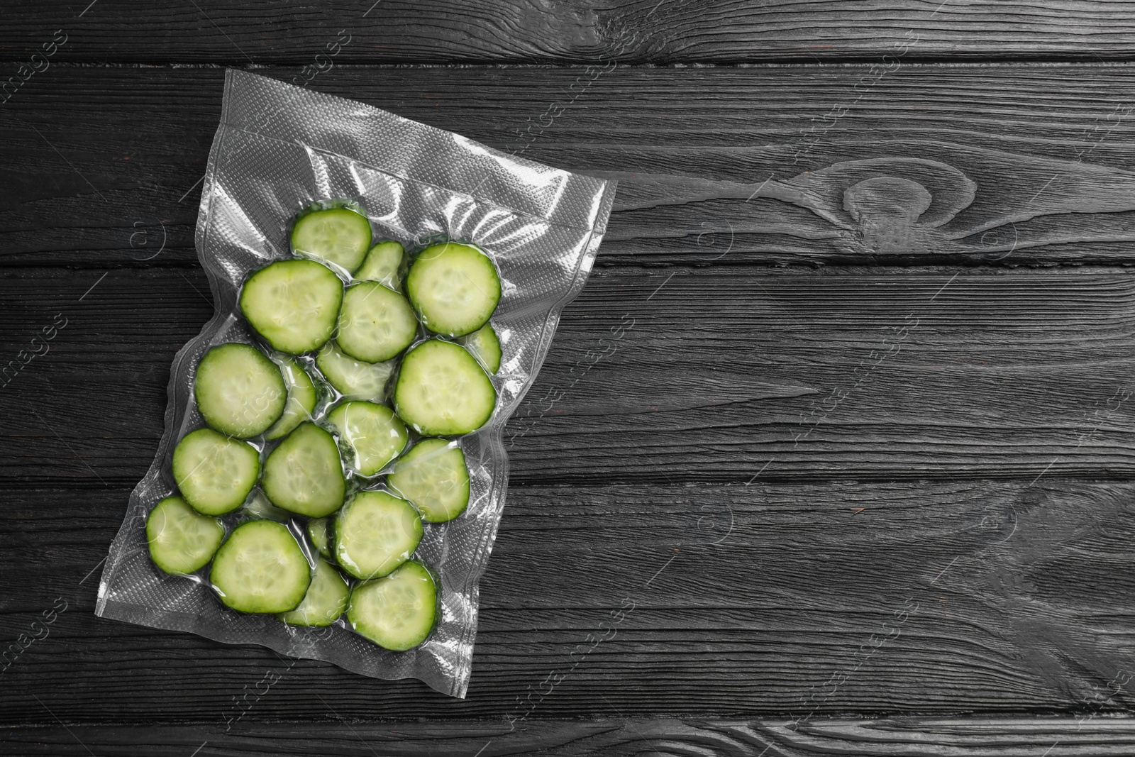 Photo of Vacuum pack of cucumbers on black wooden table, top view. Space for text