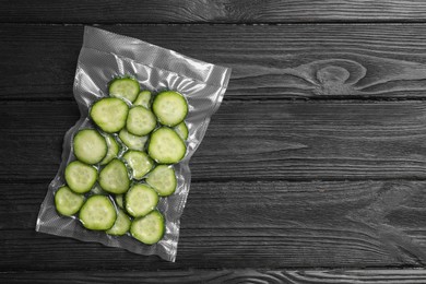 Photo of Vacuum pack of cucumbers on black wooden table, top view. Space for text