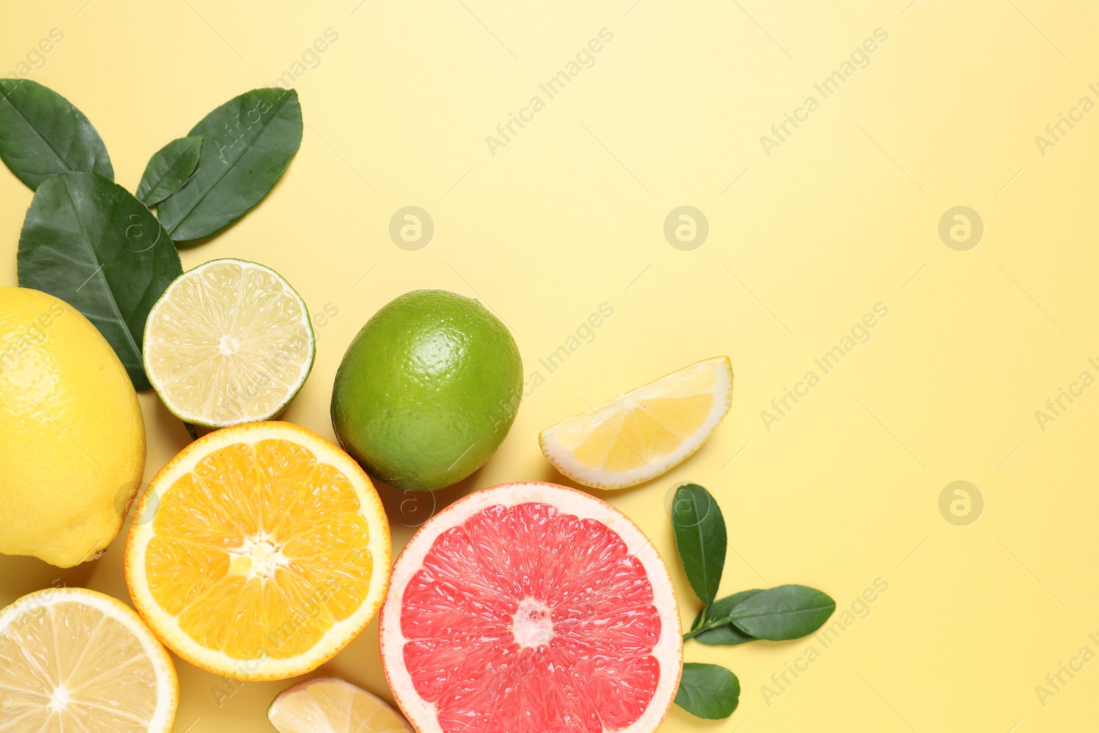 Photo of Different cut and whole citrus fruits on yellow table, flat lay. Space for text