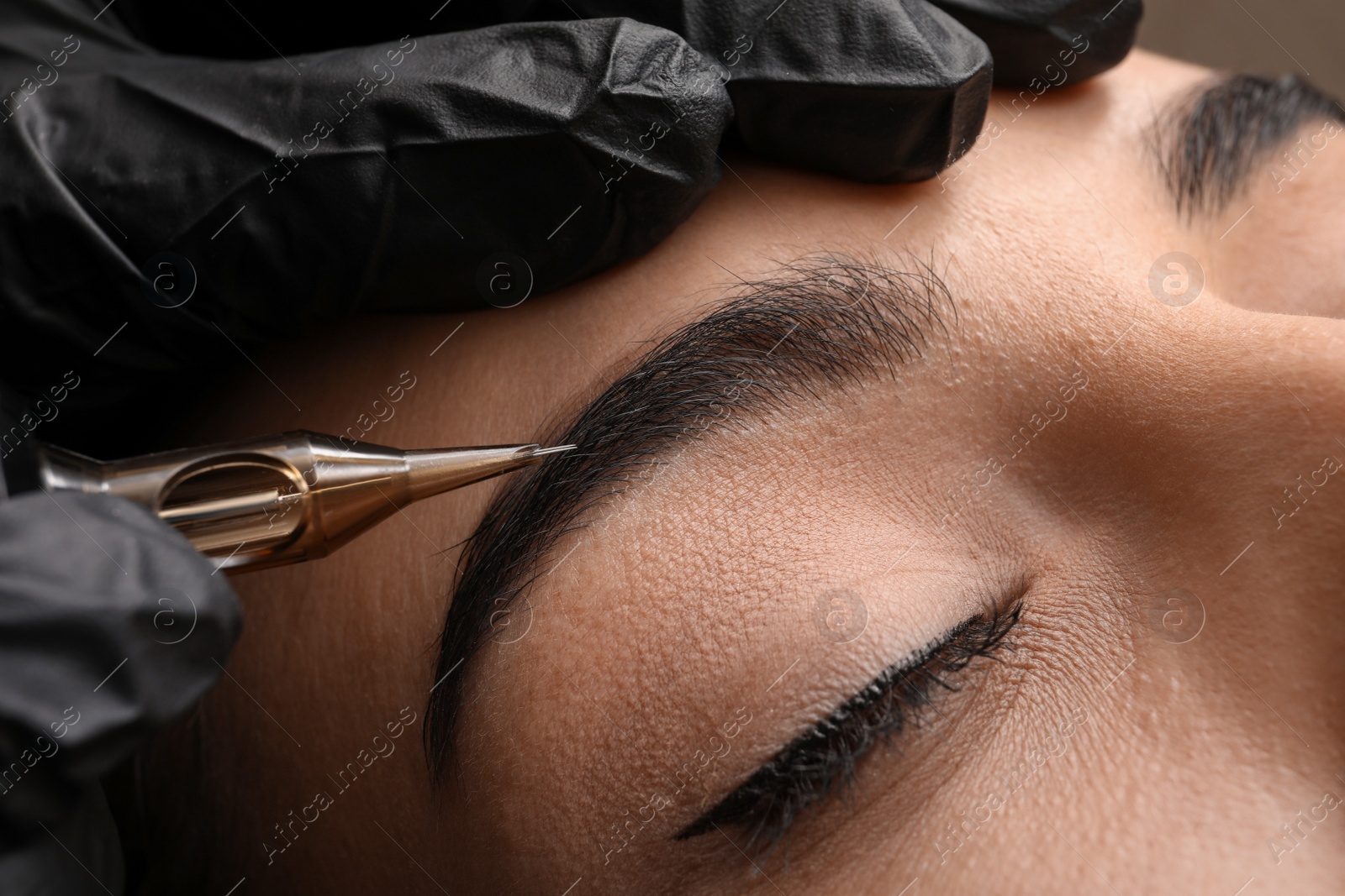 Photo of Young woman undergoing procedure of permanent eyebrow makeup in tattoo salon, closeup