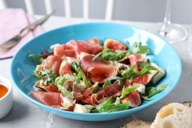 Photo of Salad with ripe figs and prosciutto served on grey marble table indoors, closeup