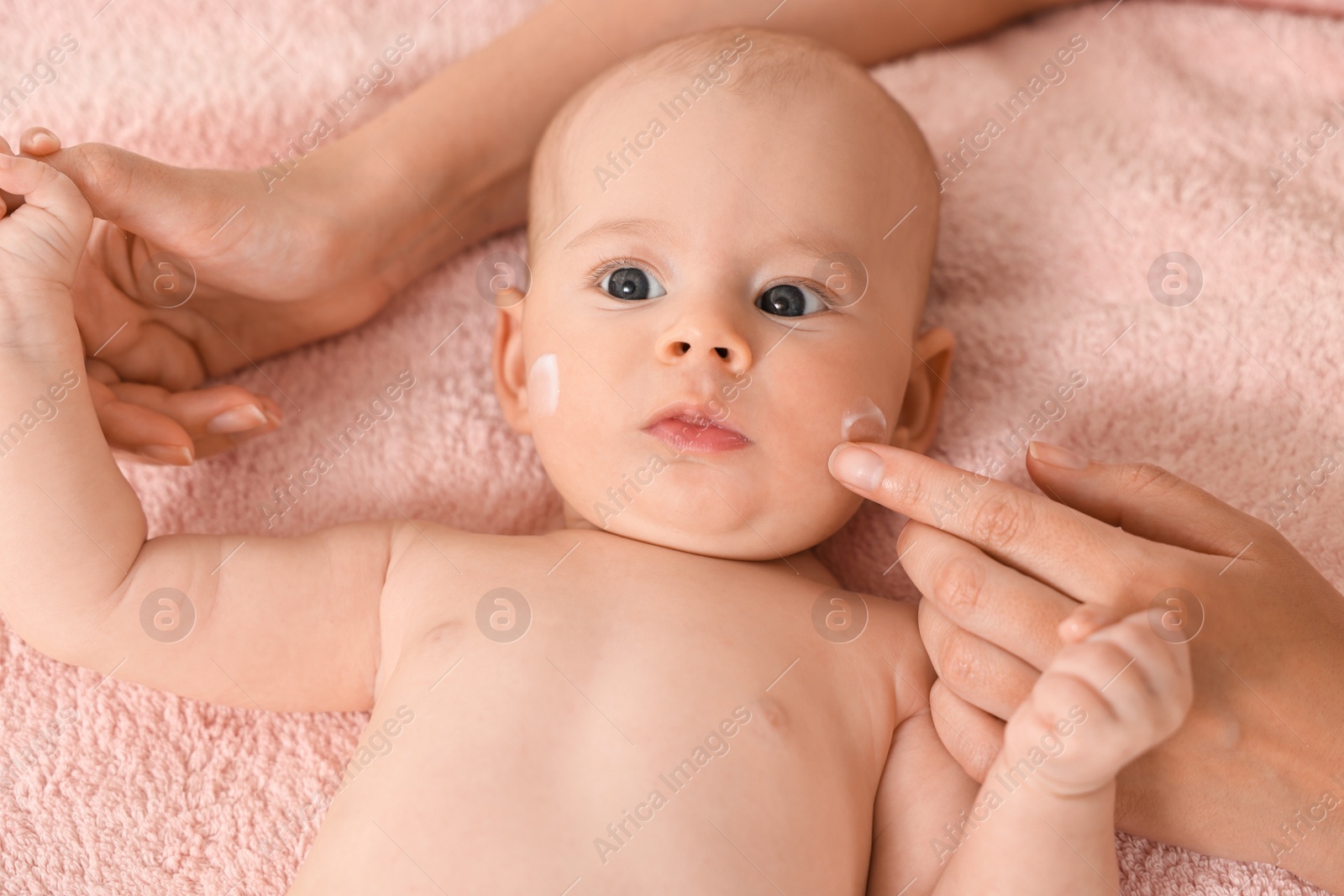 Photo of Woman applying cream onto baby`s face on bed, closeup