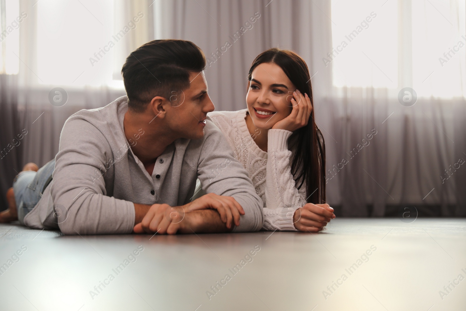 Photo of Happy couple lying on warm floor at home. Heating system