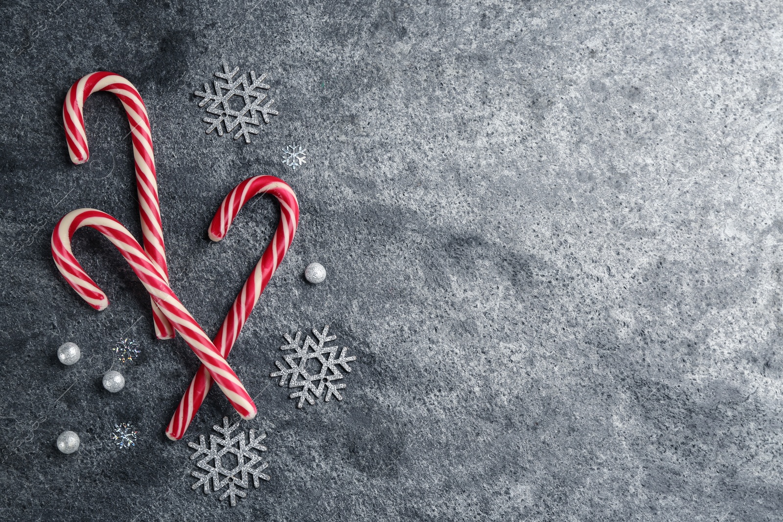 Photo of Candy canes and snowflakes on grey table, flat lay with space for text. Christmas treat