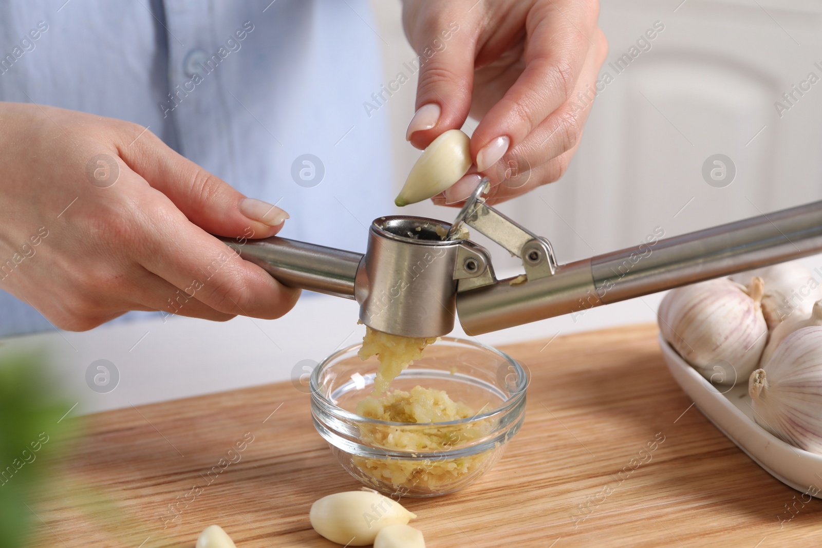 Photo of Woman squeezing garlic with press at wooden table, closeup