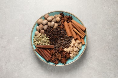 Different spices and nuts in bowl on light gray textured table, top view