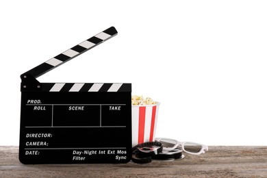 Photo of Movie clapper, bucket of tasty popcorn, glasses and film reel on wooden table against white background, space for text