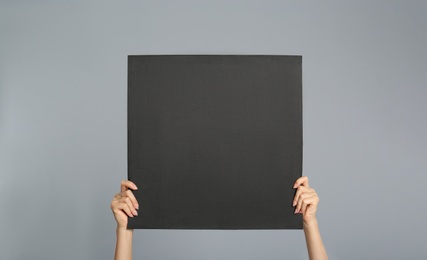 Photo of Woman holding black blank poster on grey background, closeup. Mockup for design