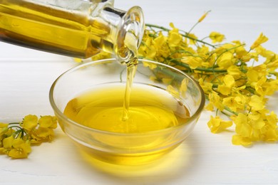 Photo of Pouring rapeseed oil into bowl at white wooden table, closeup