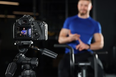 Photo of Man recording workout at gym, focus on camera. Online fitness trainer