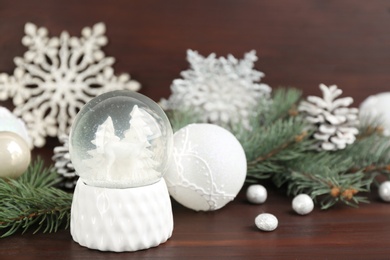 Beautiful snow globe and Christmas decor on brown wooden table, space for text