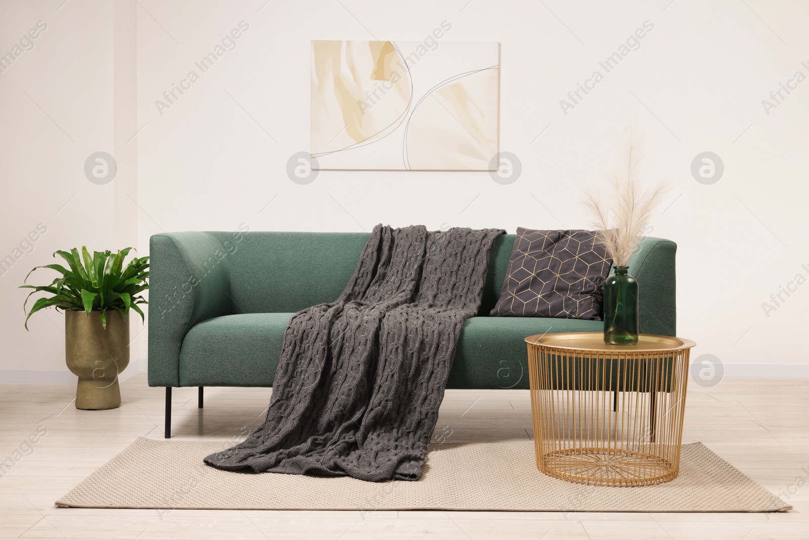 Photo of Stylish living room interior with comfortable sofa, blanket, houseplant and side table