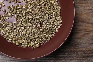 Photo of Plate of gold nuggets on wooden table, top view