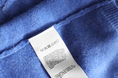 Photo of Clothing label in different languages on blue garment, closeup